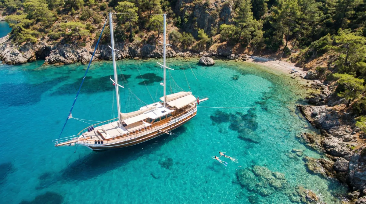 Aerial view of a luxury gulet anchored in a secluded turquoise cove with people swimming