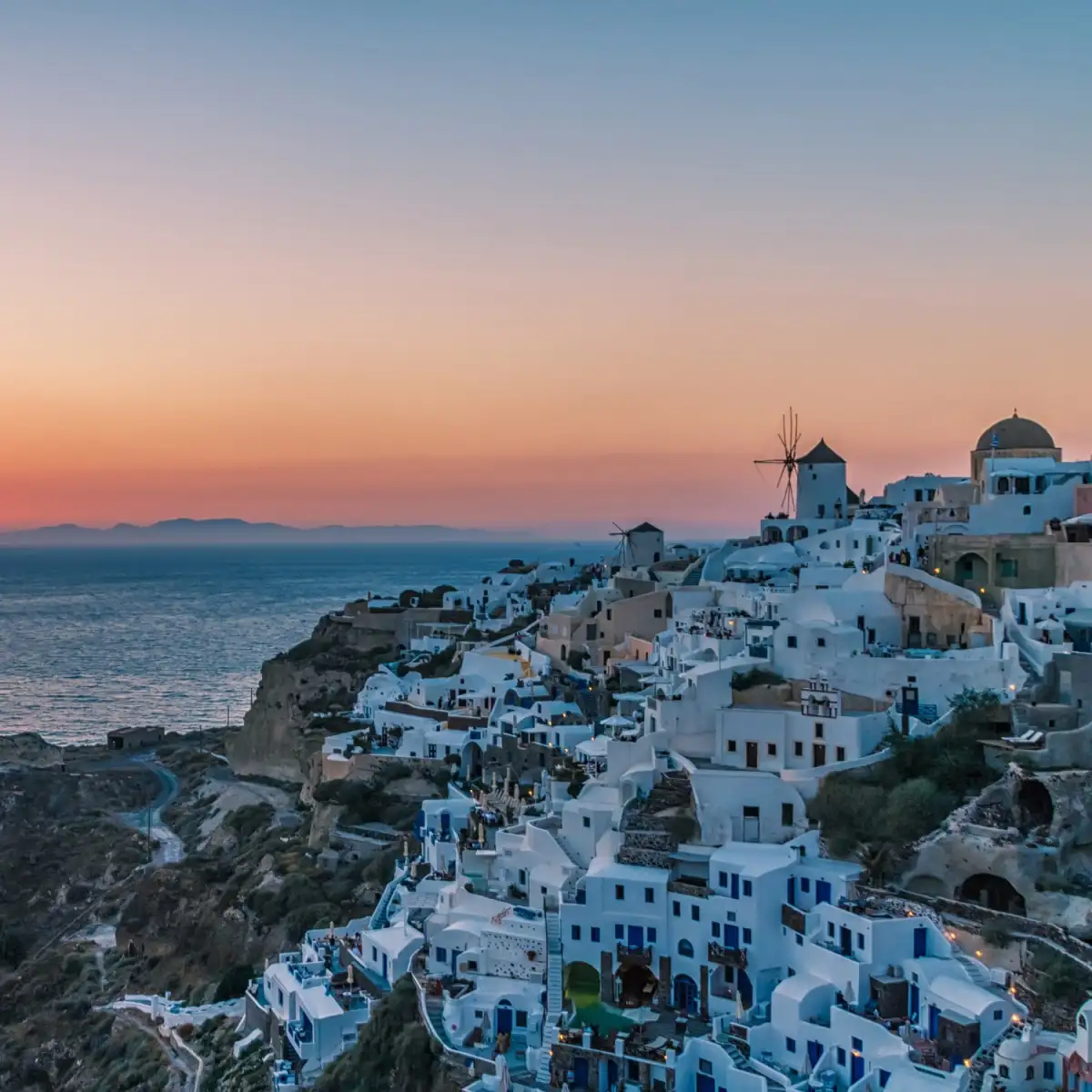 Sunset at Oia village in Santorini - one of the most popular stops on island hopping routes. The white-washed houses and blue-domed churches create a stunning vista over the turquoise waters of the Aegean Sea.